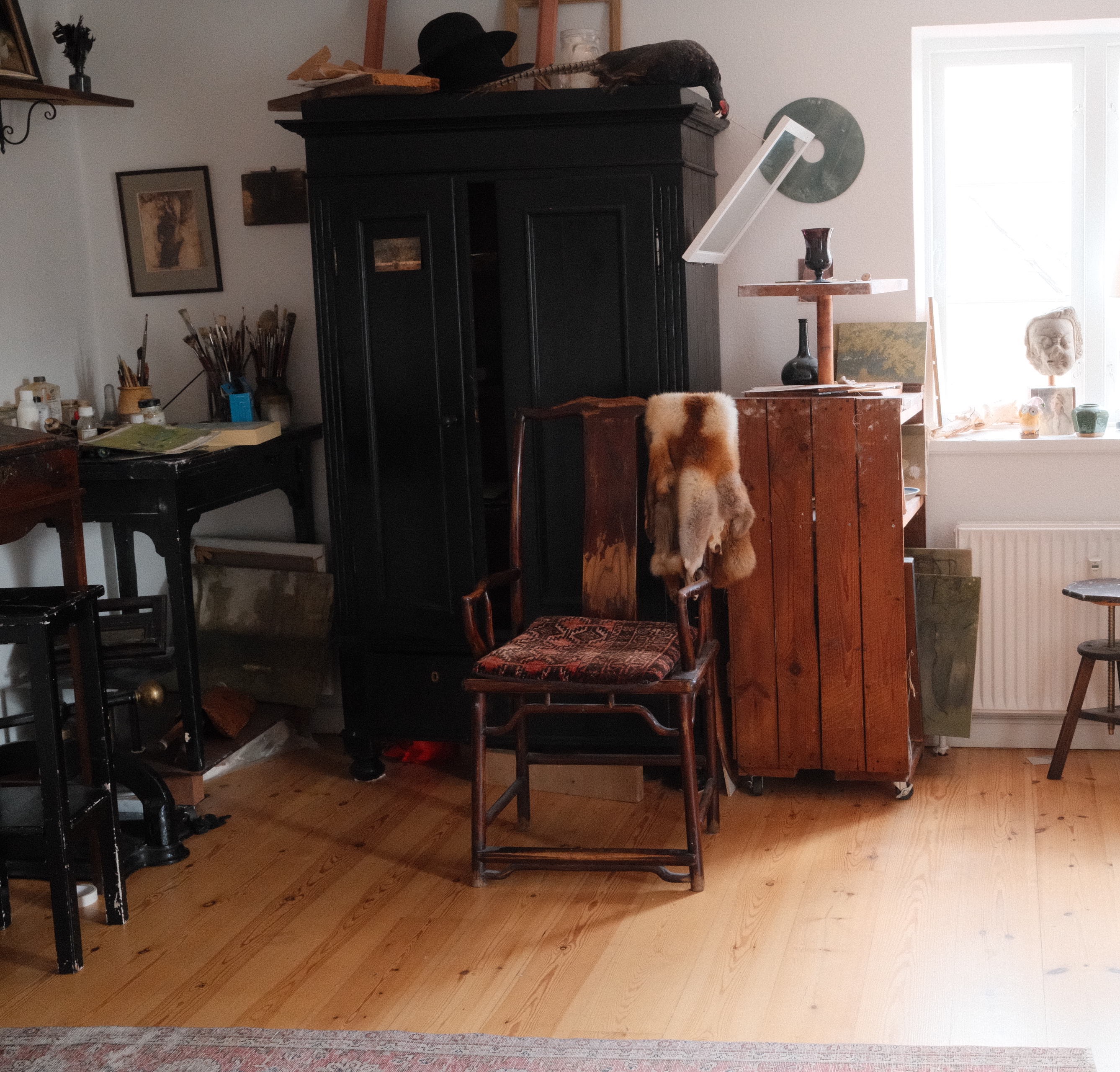 The atelier, with a black armoire, an antique chair, easels and plaster casts by the window.